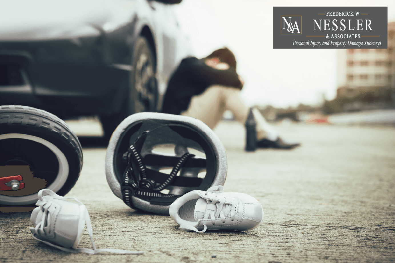 Man sitting and leaning with his head in his arms against a black car and in the foreground you see a helmet and shoe on the street depicting a car crash